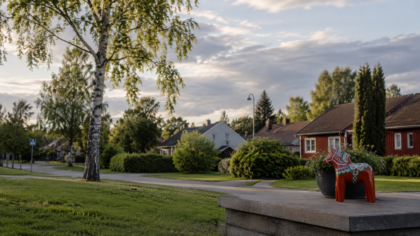Villakvarter i Avesta en sommarkväll med röd trävilla, björk och en dalahäst i förgrunden